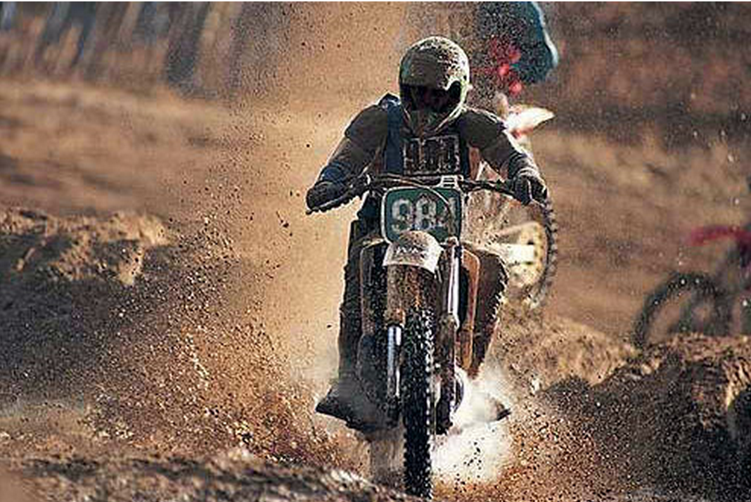 A person riding a dirt bike is covered in mud